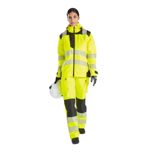 Vrouw in signaalgele werkkleding. Ze houdt een helm in haar hand en kijkt recht in de camera. Er is een link naar de PW3 high-visibility regenbroek voor dames PW386 toegevoegd.