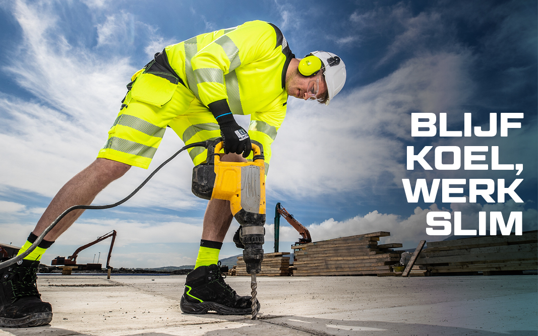 Arbeider met helm en gehoorbescherming in goed zichtbare gele zomerwerkkleding aan het werk met een drilboor, op de achtergrond blauwe, licht bewolkte lucht, graafmachine en stapel houten planken.