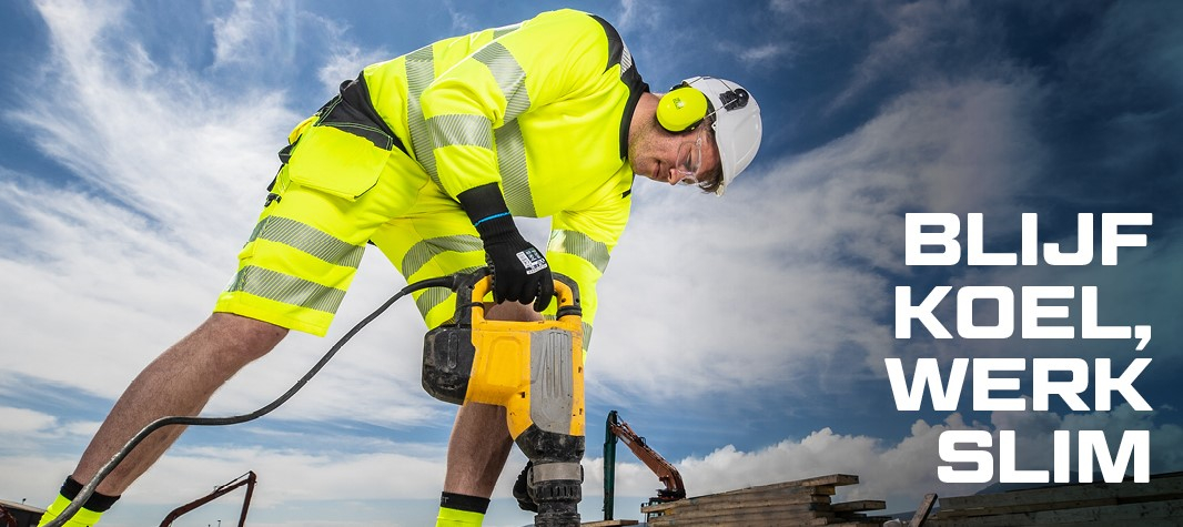 Arbeider met helm en gehoorbescherming in goed zichtbare gele zomerwerkkleding aan het werk met een drilboor, op de achtergrond blauwe, licht bewolkte lucht, graafmachine en stapel houten planken.