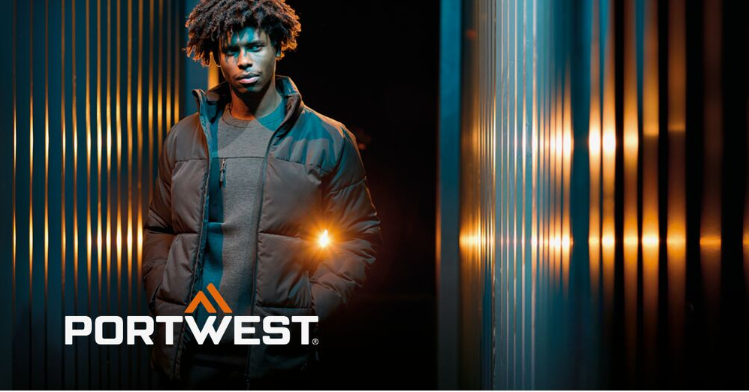 Een werknemer in zwarte werkkleding tegen een abstracte achtergrond met een gestreepte muur en lichtreflecties. Het logo van de fabrikant, Portwest, in wit en oranje, bevindt zich in de linkerbenedenhoek van de afbeelding.