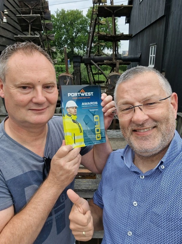 Sjoerd Kusters en Patrick Kits tegen een landelijke achtergrond. De mannen glimlachen de camera in, Sjoerd houdt de gouden plaquette in zijn handen, Patrick steekt zijn rechterduim omhoog.